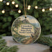 A round ornament with a scenic landscape featuring a mountain, river, and wildlife, including a deer, is displayed in front of a blurred background with Christmas lights.