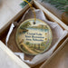 A decorative ornament in a box, featuring a scenic landscape with a bird, a canoe, and a body of water.