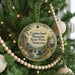 A round ornament hanging on a Christmas tree, featuring a scenic landscape with a waterfall and a cabin.
