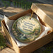 A decorative ornament in a box, featuring a scenic landscape with a waterfall and trees, with the text "Cumberland Mountain State Park, Tennessee" printed on it.