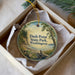 A round ornament with a scenic image of Dash Point State Park, Washington, displayed in a box with a white tissue paper lining.