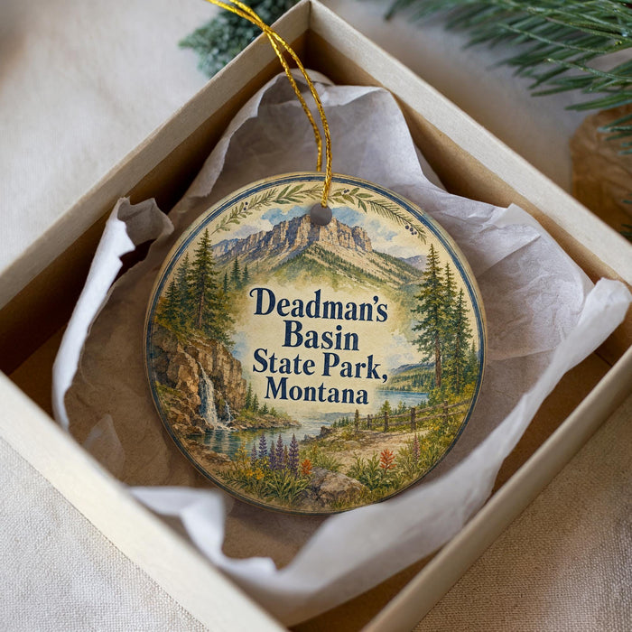 A decorative ornament in a box, featuring a scenic landscape with mountains, trees, and a river.