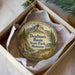 A decorative ornament in a box, featuring a scenic landscape with mountains, trees, and a river.