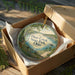 A circular ornament in a box, featuring a scenic image of Deer Creek State Park, Ohio.