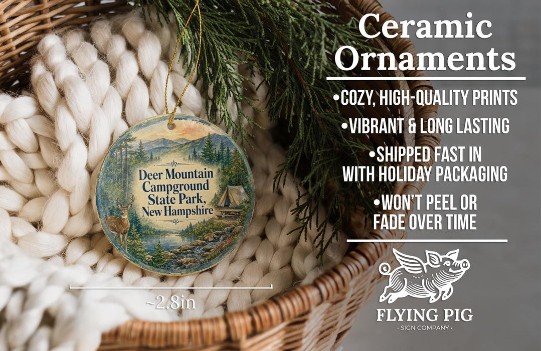 Ceramic ornaments, featuring a deer mountain campsite, are displayed in a basket with pine branches.