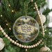A round ornament hanging on a Christmas tree, featuring a scenic landscape with a lake, bridge, and cabin.