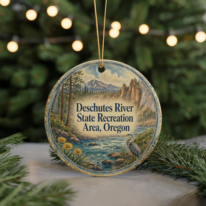 A circular ornament with a scenic landscape depicting a river, mountains, and trees, hanging from a string.