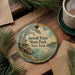 A round ornament with a scenic image of DeWolf Point State Park, New York, hangs on a wooden surface.