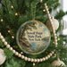 A round ornament hanging on a Christmas tree, featuring a scenic landscape with a lake and trees.
