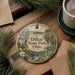 A decorative ornament with a scenic image of a waterfall and forest, featuring the text "Dillon State Park, Ohio" on it, is displayed on a wooden surface alongside a cup of coffee and some pine branches.