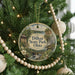 A round ornament hanging on a Christmas tree, featuring a scenic landscape with a waterfall and a cabin.