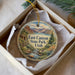 A decorative ornament in a box, featuring a scenic landscape with mountains, a river, and a cabin.