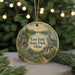 A round ornament with a scenic landscape featuring a lake, a house, and a bird, hanging from a string.