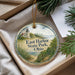 A decorative ornament with a lighthouse and a coastal scene, placed in a box with pine branches.