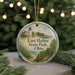 A round ornament with a lighthouse and a scenic landscape, featuring the text "East Harbor State Park, Ohio" on it, is displayed on a table with pine branches in the background.