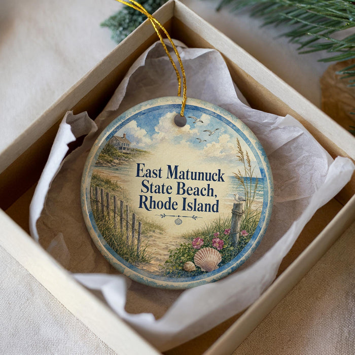 A decorative ornament in a box, featuring a beach scene with a wooden fence, seashells, and a bird in flight.