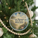 A round ornament hanging on a Christmas tree, featuring a beach scene with a path leading to a house.