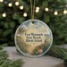 A round ornament with a beach scene and text, hanging on a string.