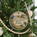 A round ornament hanging on a Christmas tree, featuring a scenic landscape with a house and trees.