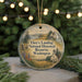 A circular ornament with a scenic landscape and text, hanging on a string.