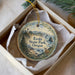 A decorative ornament in a box, featuring a scenic landscape with mountains, trees, and a lighthouse, with the text "Ecola State Park, Oregon" printed on it.