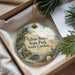 A decorative ornament with a beach scene and a bird, placed in a box with pine branches.