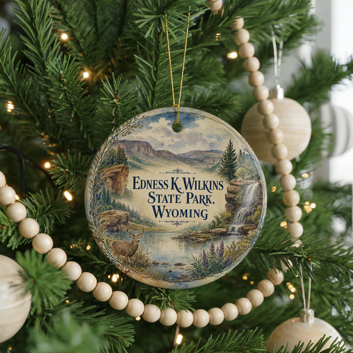 A round ornament hanging on a Christmas tree, featuring a scenic landscape with mountains, a waterfall, and a deer.