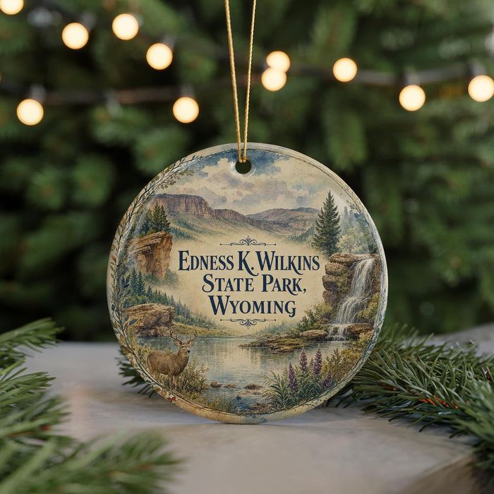 A decorative ornament featuring a scenic landscape with mountains, a waterfall, and a deer, hanging from a string.