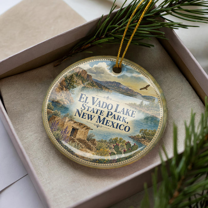 A decorative ornament with a landscape scene featuring El Vado Lake, State Park, New Mexico, is displayed in a box with pine branches.