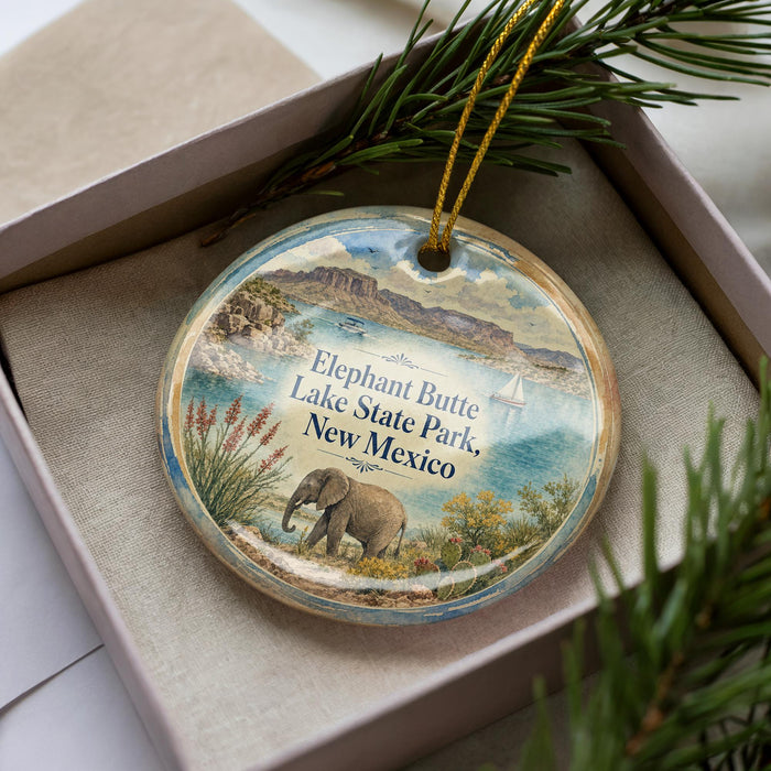 A decorative ornament in a box, featuring an elephant and a scenic landscape with mountains, water, and a sailboat.