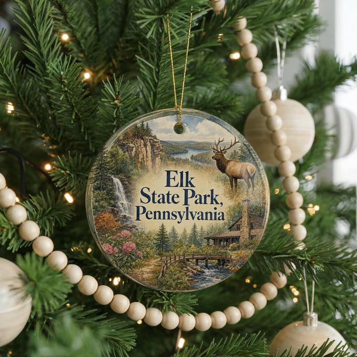 A round ornament hanging on a Christmas tree, featuring a scenic landscape with a waterfall, a bridge, and a deer.