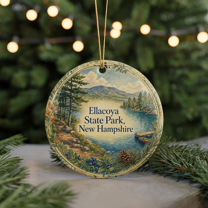 A round ornament with a scenic landscape of Ellacoya State Park, New Hampshire, featuring a lake, mountains, and pine trees.