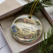 A decorative ornament in a box, featuring a landscape with a mountain, trees, and flowers, along with the text "Enchanted Rock State Natural Area, Texas".