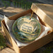 A decorative ornament in a box, featuring a scenic landscape with a waterfall and pine trees, with the text "Evanston State Park, New York" printed on it.
