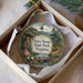 A decorative ornament in a box, featuring a scenic landscape with a bridge, trees, and a body of water.