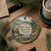 A decorative ornament featuring a scenic landscape with a stone formation, surrounded by pine trees and a winding path, placed on a wooden surface next to a cup of coffee.
