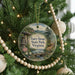 A round ornament hanging on a Christmas tree, featuring a scenic landscape with a bridge and mountains in the background.