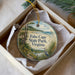 A decorative ornament in a box, featuring a scenic landscape with a path, a bird, and a body of water.