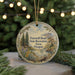 A round ornament with a scenic landscape and text, hanging on a string.
