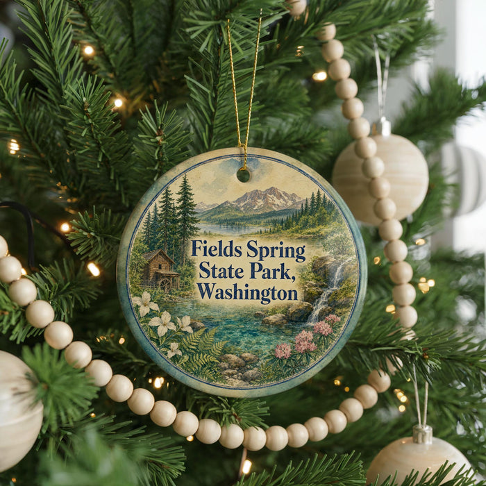 A circular ornament hanging on a Christmas tree, featuring a scenic landscape with mountains, a lake, and a cabin.