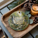 A decorative ornament featuring a scenic image of Fillmore Glen State Park, New York, with a candle and pine cones on a wooden tray.