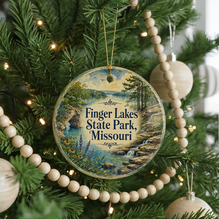 A round ornament hanging on a Christmas tree, featuring a scenic landscape with a lake and mountains.