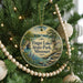 A round ornament hanging on a Christmas tree, featuring a scenic landscape with a lake and mountains.