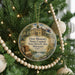 A circular ornament hanging on a Christmas tree, featuring an illustration of a historic building and surrounded by ornaments and lights.