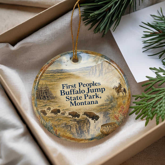 A decorative ornament in a box, featuring a scenic landscape with buffalo and a person on horseback, along with text that reads "First Peoples Buffalo Jump State Park, Montana".