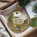 A decorative ornament with a scenic landscape of Fisher Grove State Park, South Dakota, featuring a bridge, pine trees, and a lake.