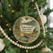 A round ornament hanging on a Christmas tree, featuring a scenic landscape with a bridge and pine trees.
