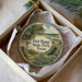A decorative ornament in a box, featuring a scenic landscape with a windmill, trees, and a body of water.