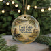 A round ornament with a painting of Fort Cobb State Park, Oklahoma, featuring a wagon and a house, is displayed on a Christmas tree.