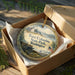 A round ornament in a box, featuring a scenic image of Fort Columbia State Park in Washington.